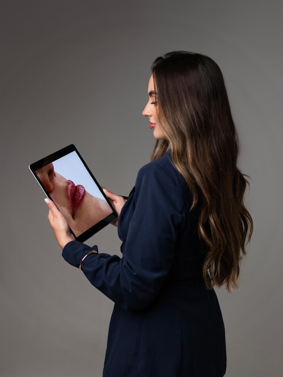 Nathalia Crestani analisando a foto de um caso de preenchimento labial no tablet.